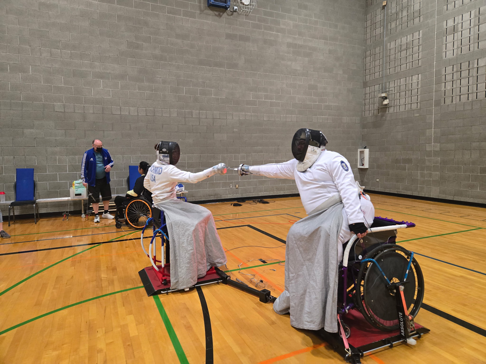 Fencers in wheelchairs spar in a gym.