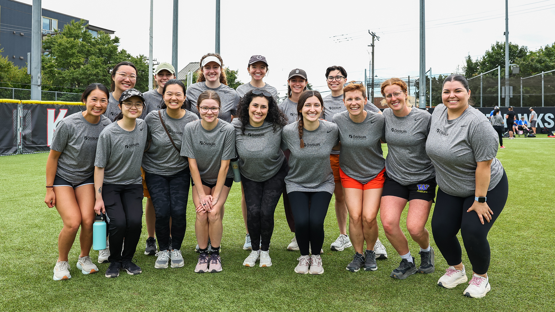 A group of people in grey t-shirts pose in a playing field.