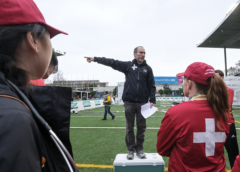 A man standing on a sports field points while talking to people wearing red cross jackets