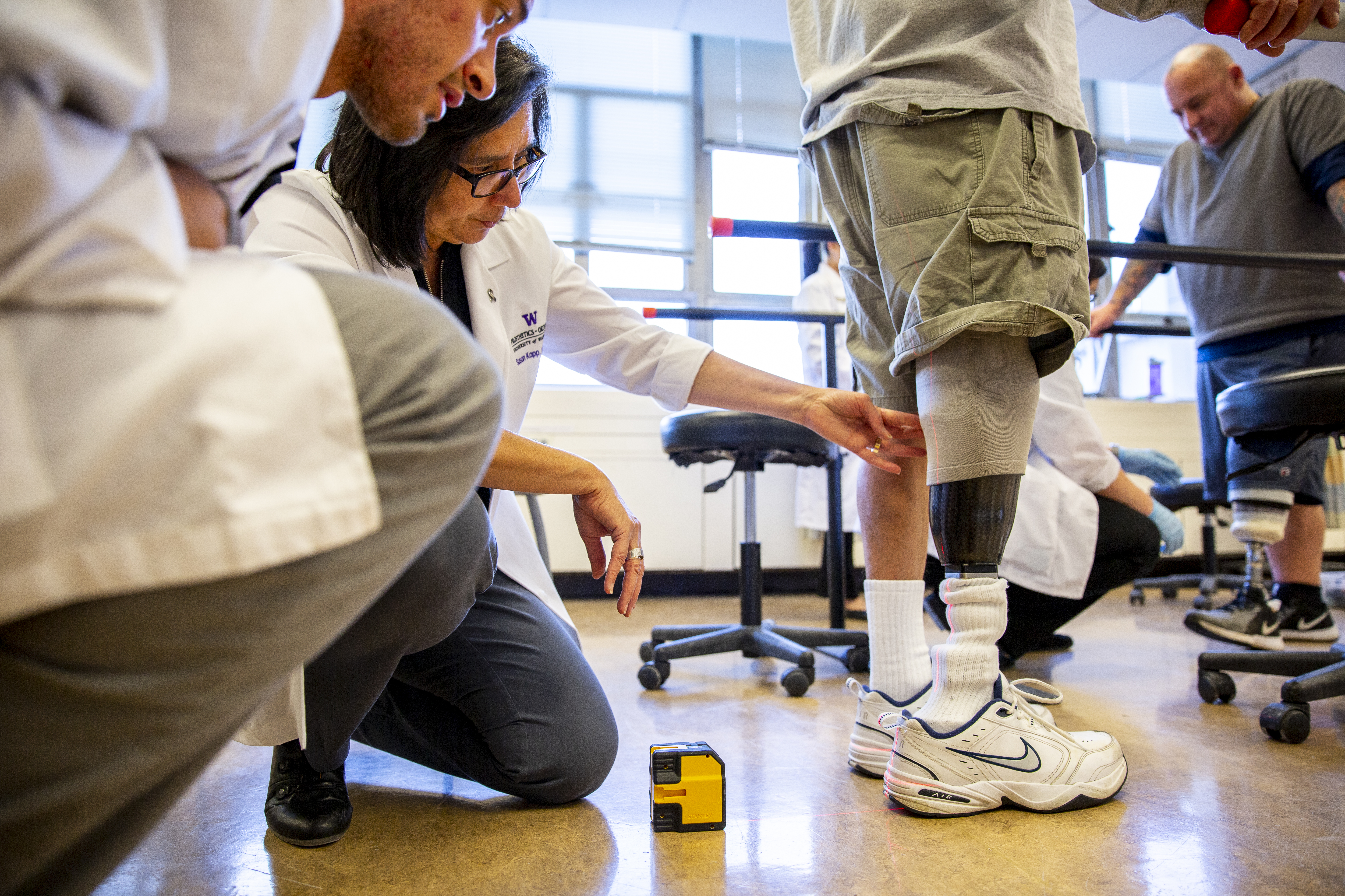 Female physician examining a prosthetic right leg on a male patient as he stands in a research lab