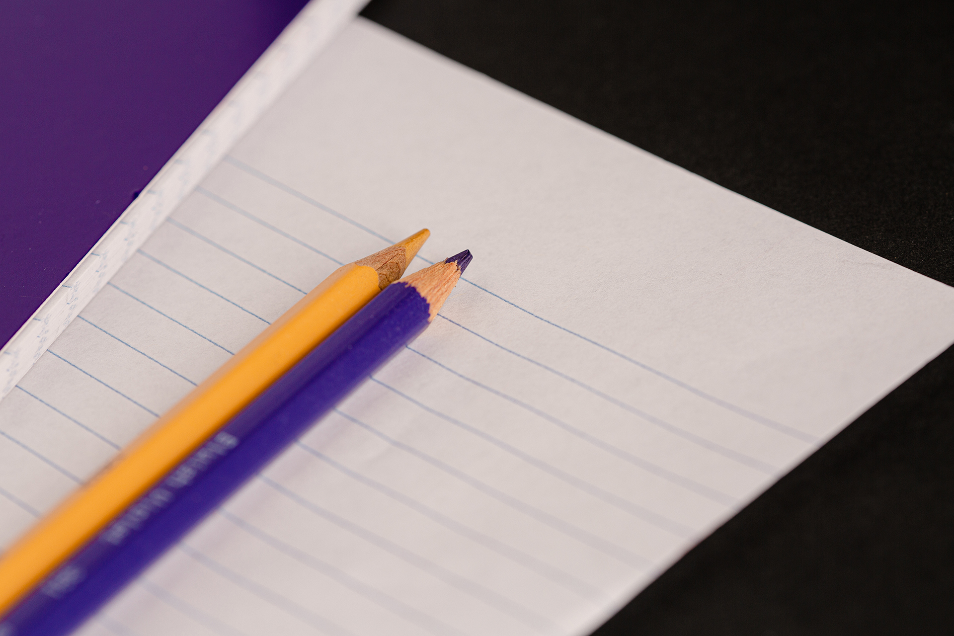 A yellow and a purple pencil rest on a blank page.