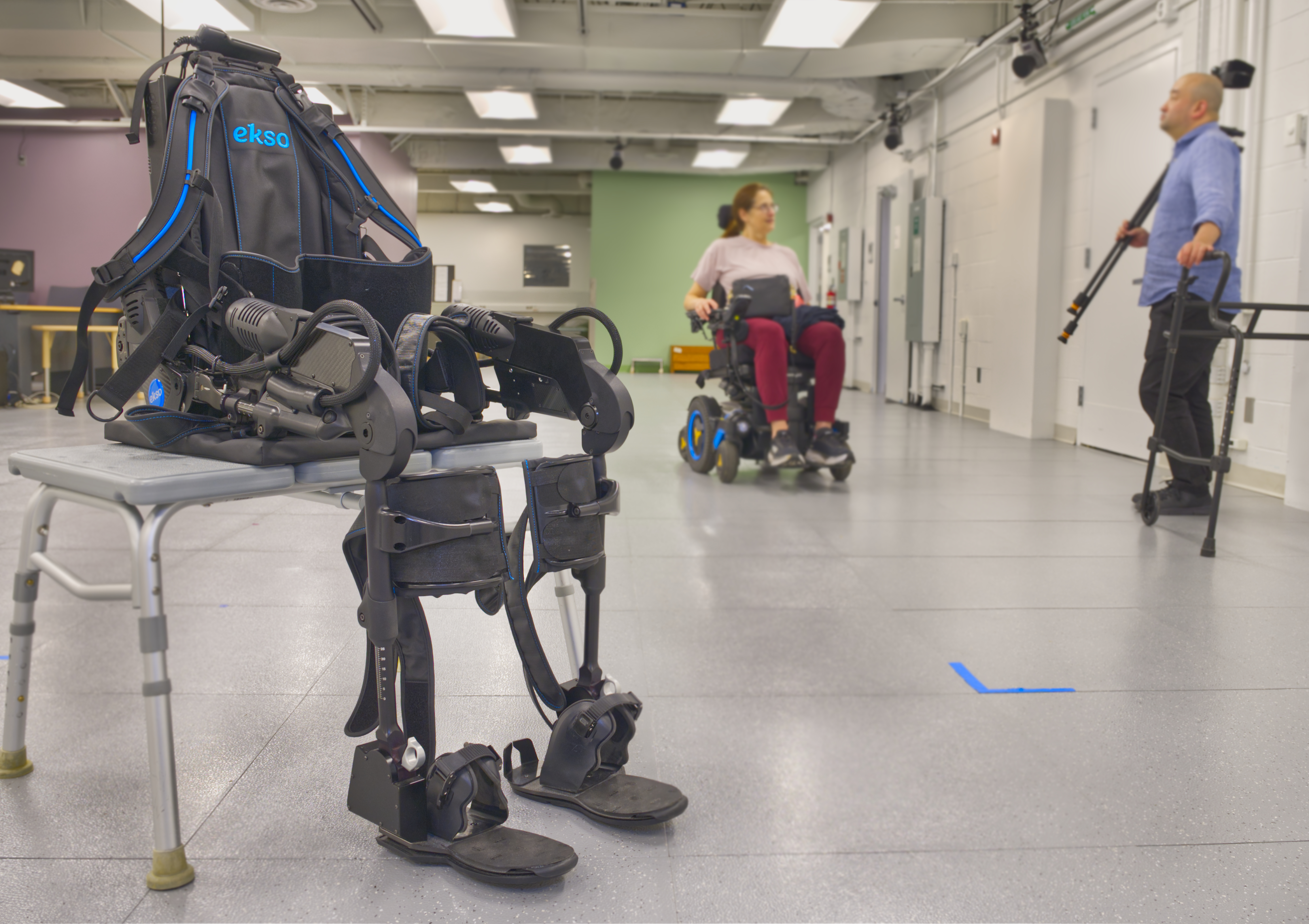 Personalized exoskeleton in foreground with female sitting in wheelchair and male researcher standing in background