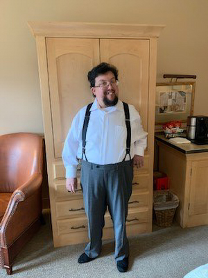 A man in a white shirt and dress pants stands in a hotel room.