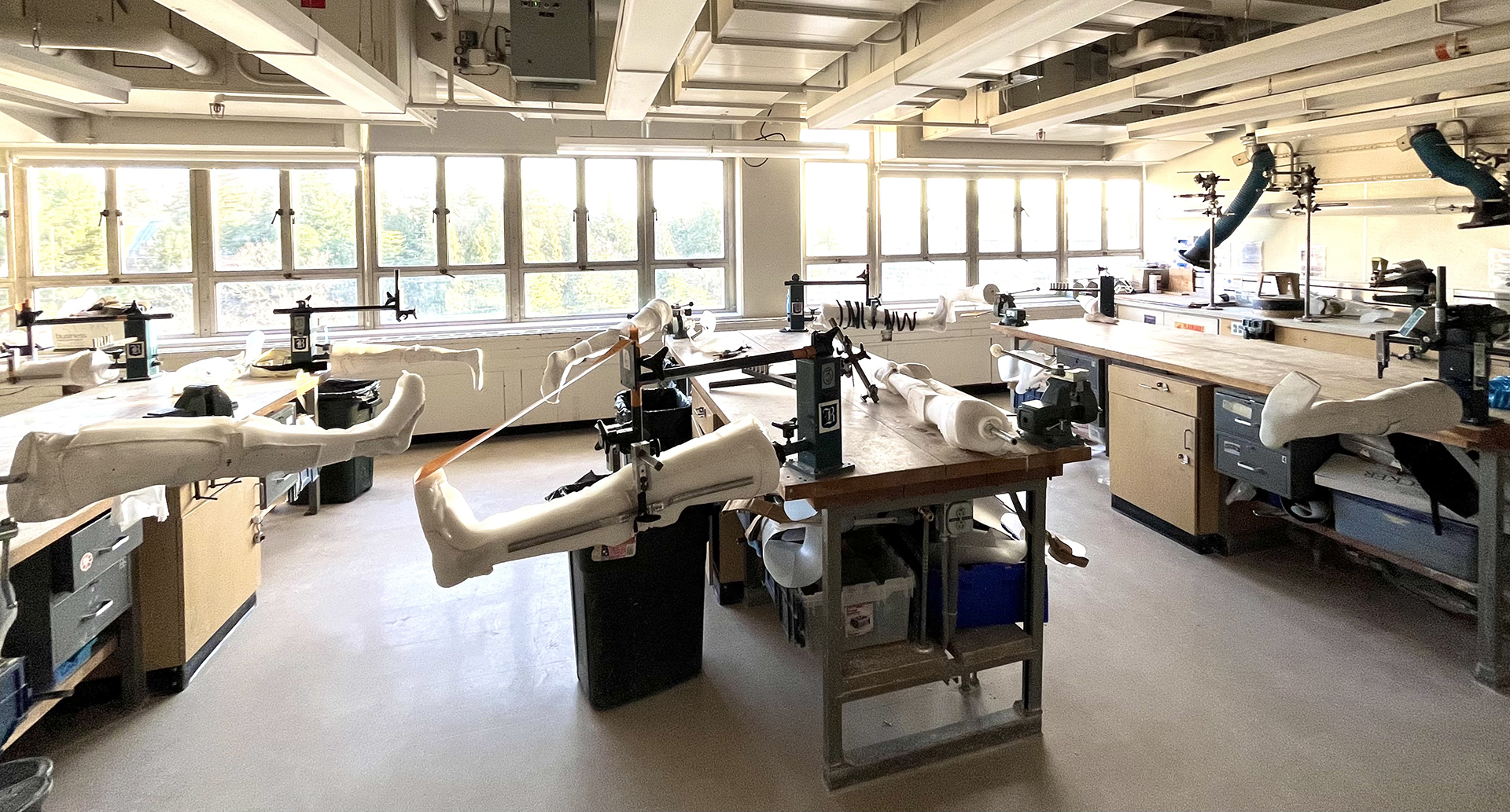 A lab, flooded with light, with several plaster legs held by clamps.