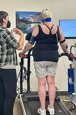 A woman assists another woman on a treadmill.