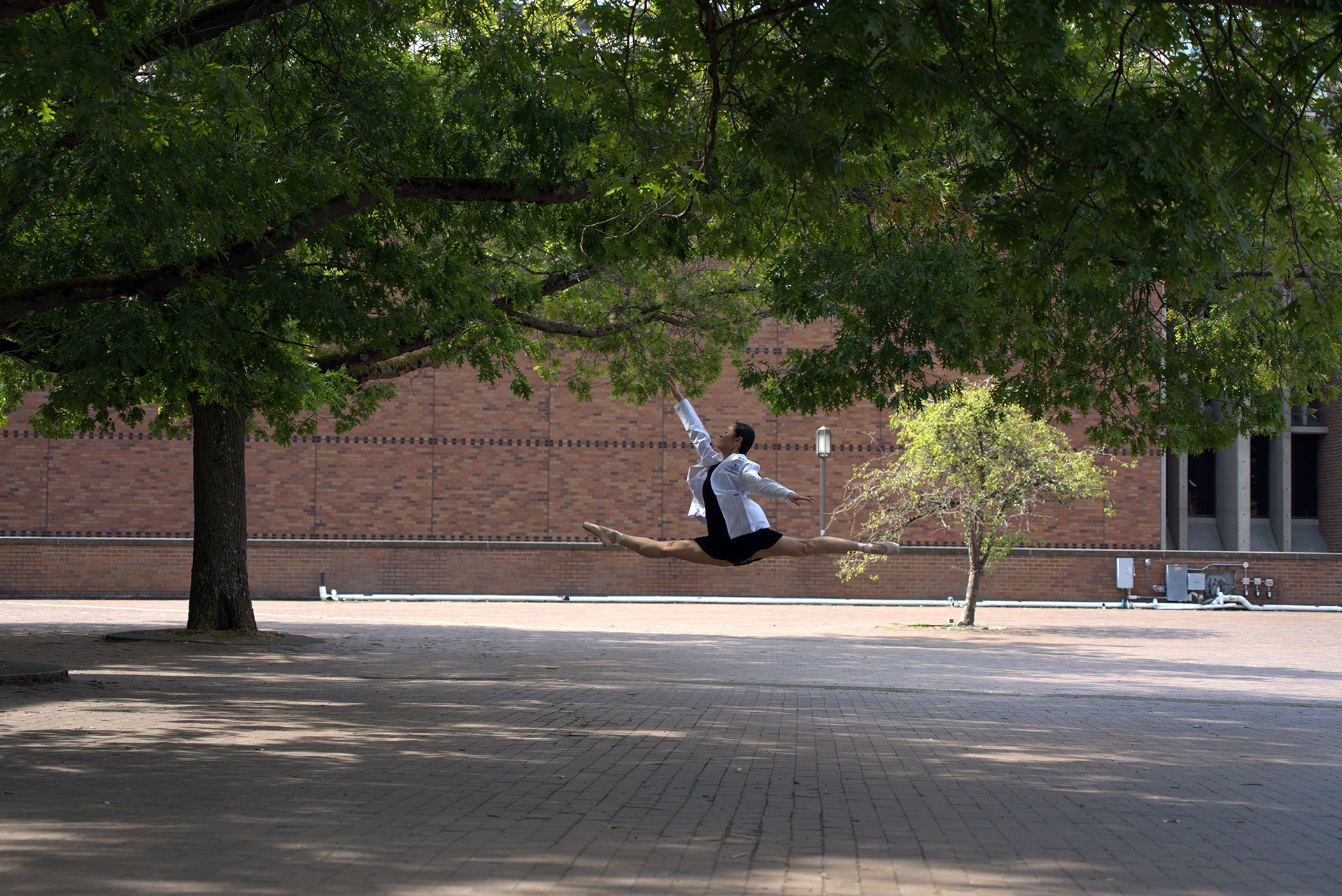 A woman in a white doctor's coat leaps into the air in a brink plaza.