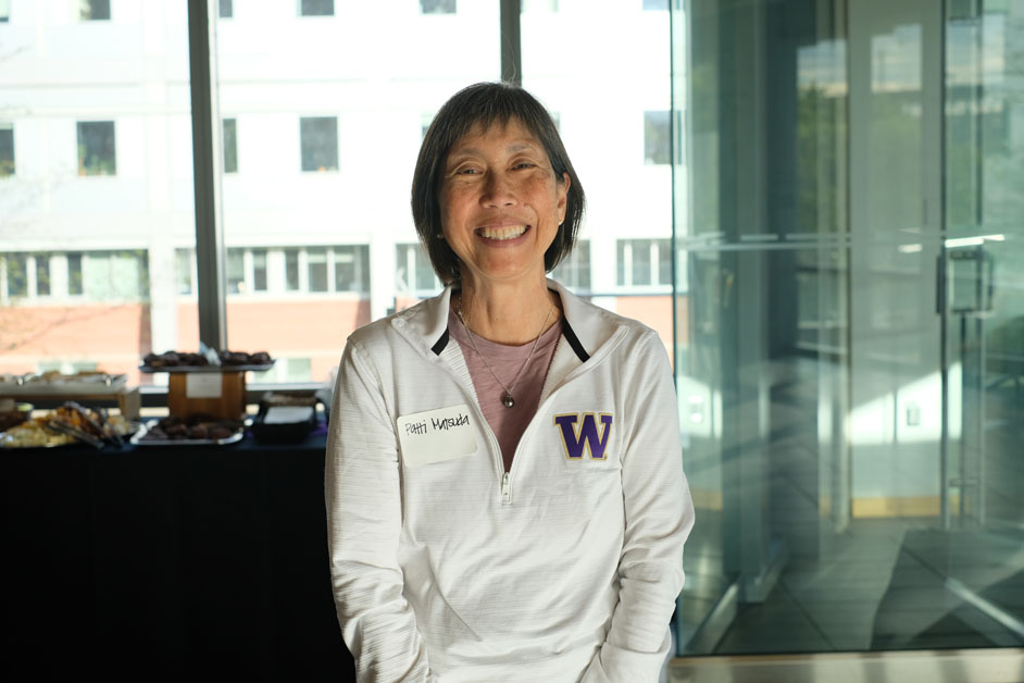 A woman wearing a white shirt with a purple W on it smiles at the camera.