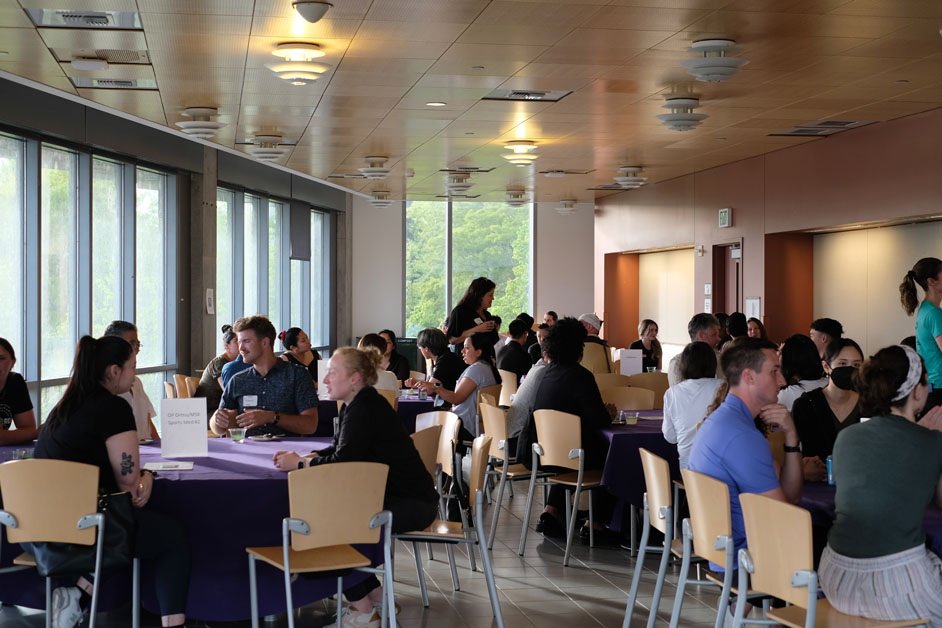 People chat at tables in a light-filled room.