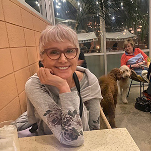 Dagmar smiles at the camera while two dogs make friends behind her.