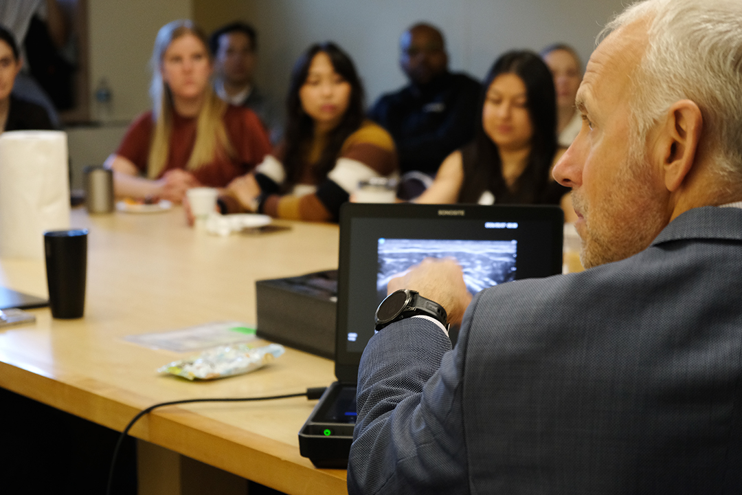 A man points at a screen showing an ultrasound image while people look on.