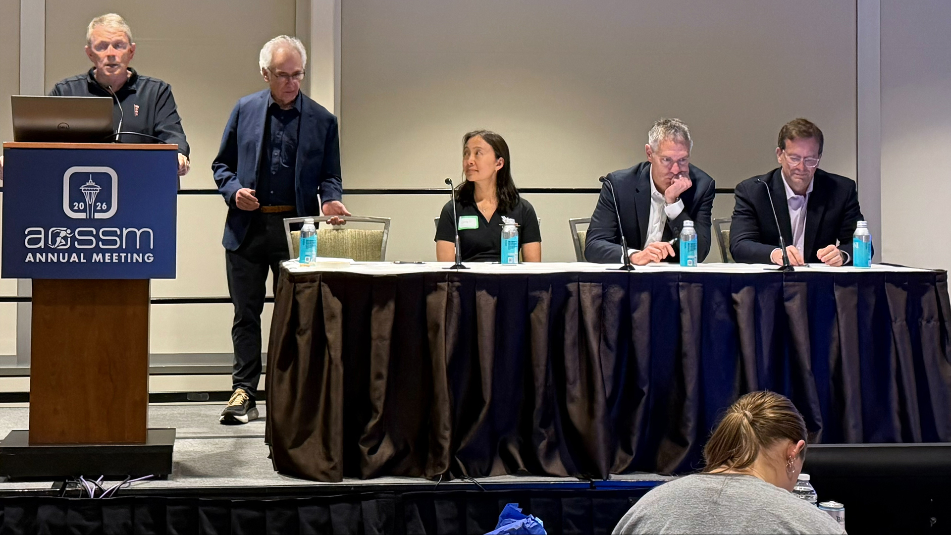 Five people present a panel presentation on a conference stage.