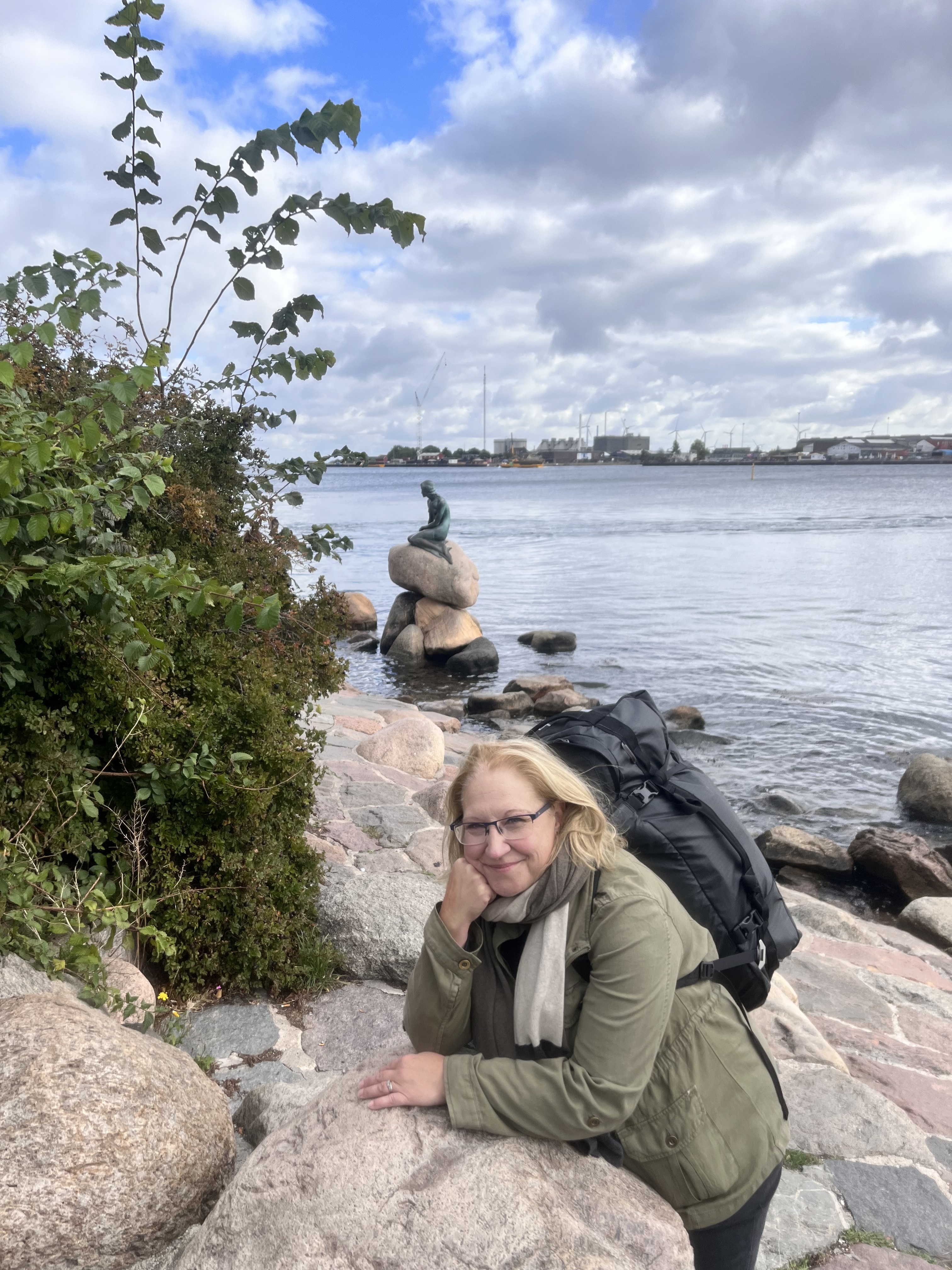 Erica stands smiling atop a rock with a green bush and water behind her