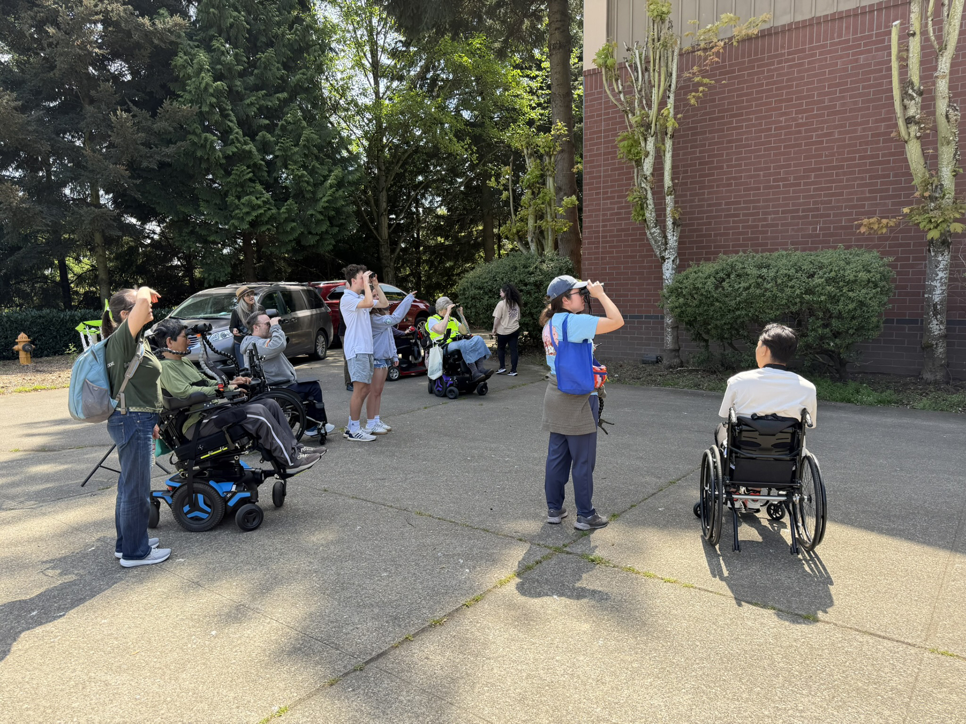 A group of people, some in wheelchairs, scan the sky with bionoculars