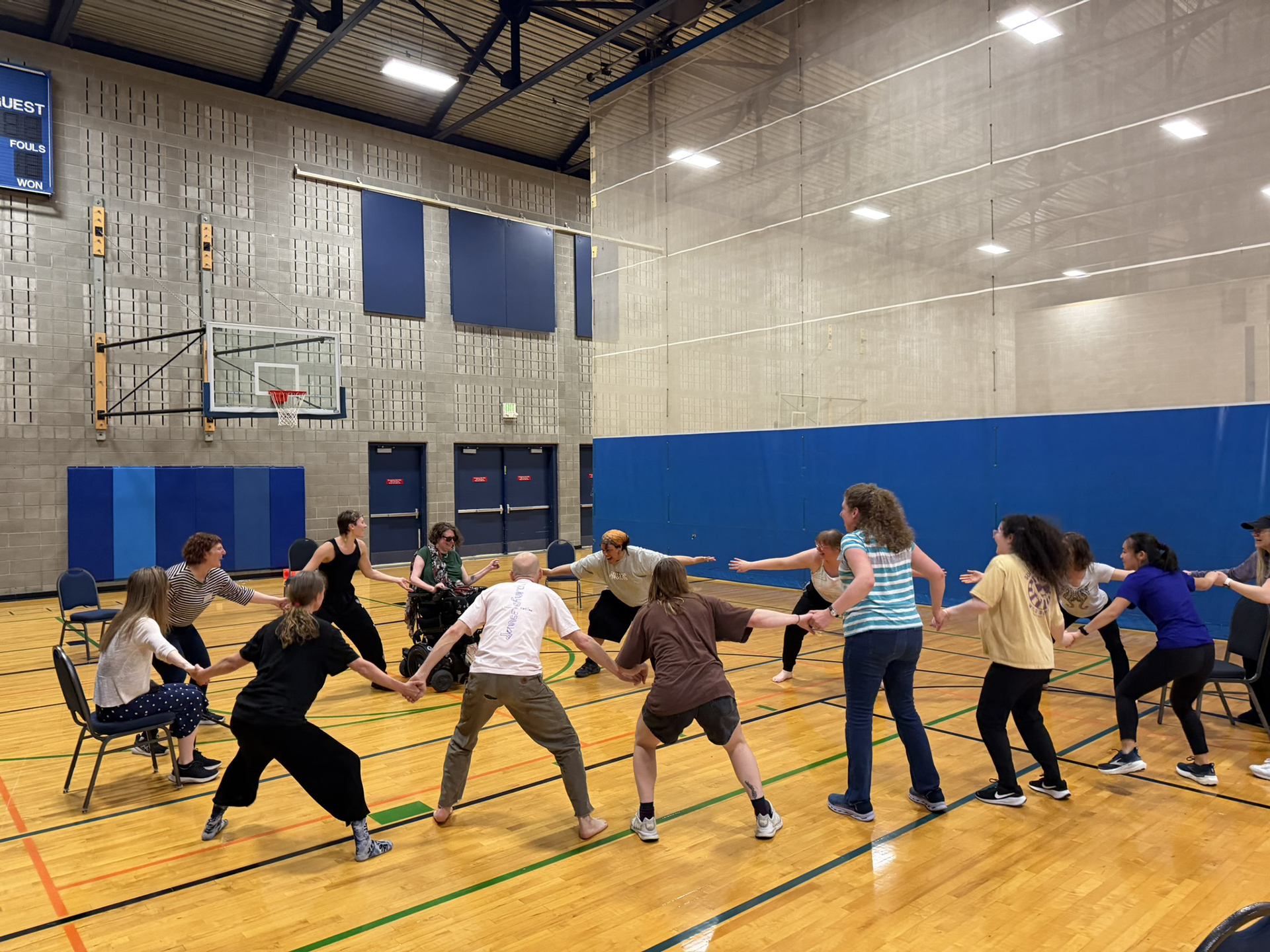A group of people, some standing, some in chairs and some in wheelchairs, dance together in a circle.