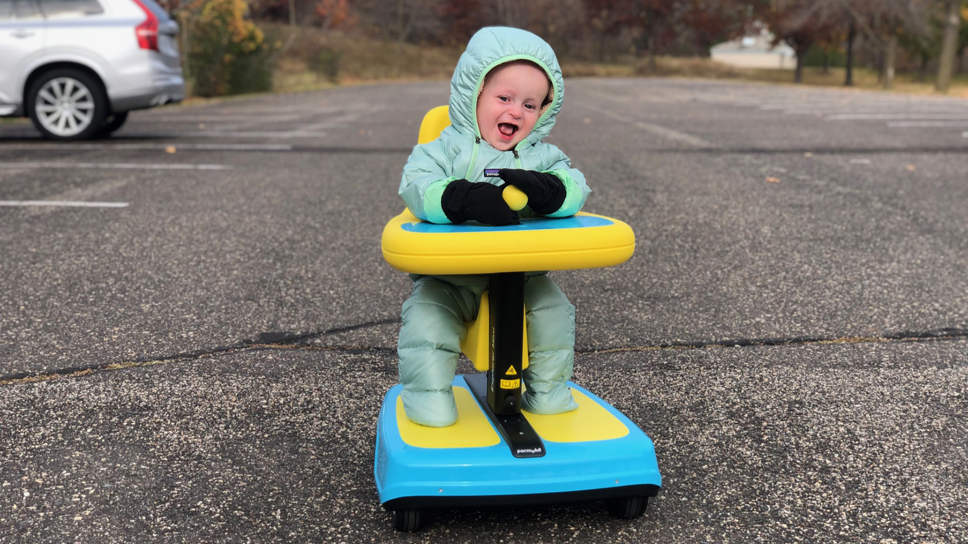 A toddler steers across a parking lot in a joystick-controlled mobility device.