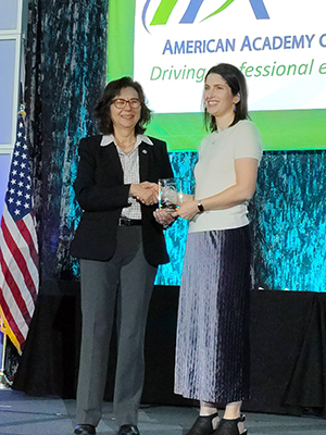 Two women shake hands on a stage.