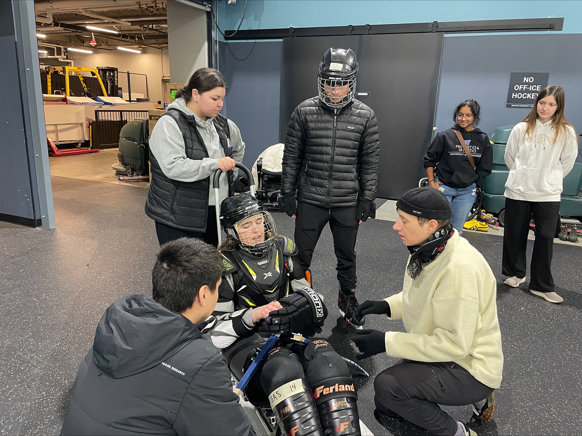 Volunteers help a woman gear up for sled hockey.