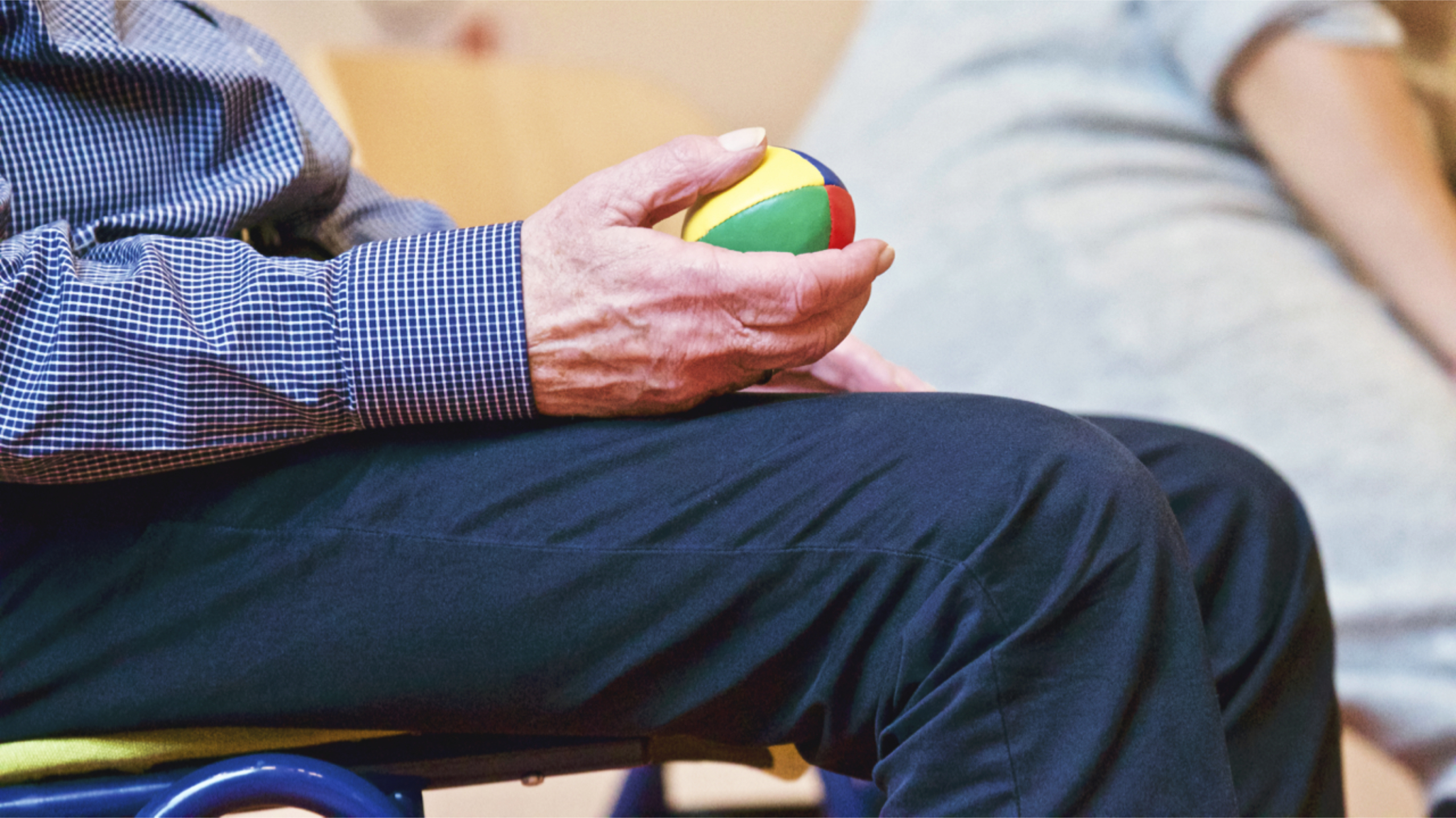 Man in blue pants and shirt holding a rubber ball in one hand while sitting in a chair