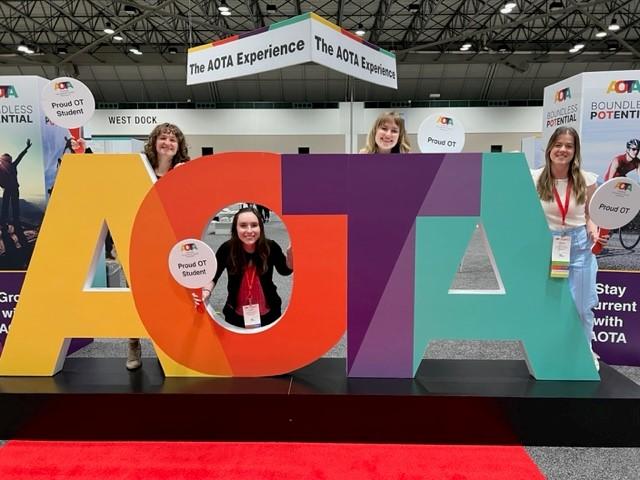 4 students posing with a large AOTA sign
