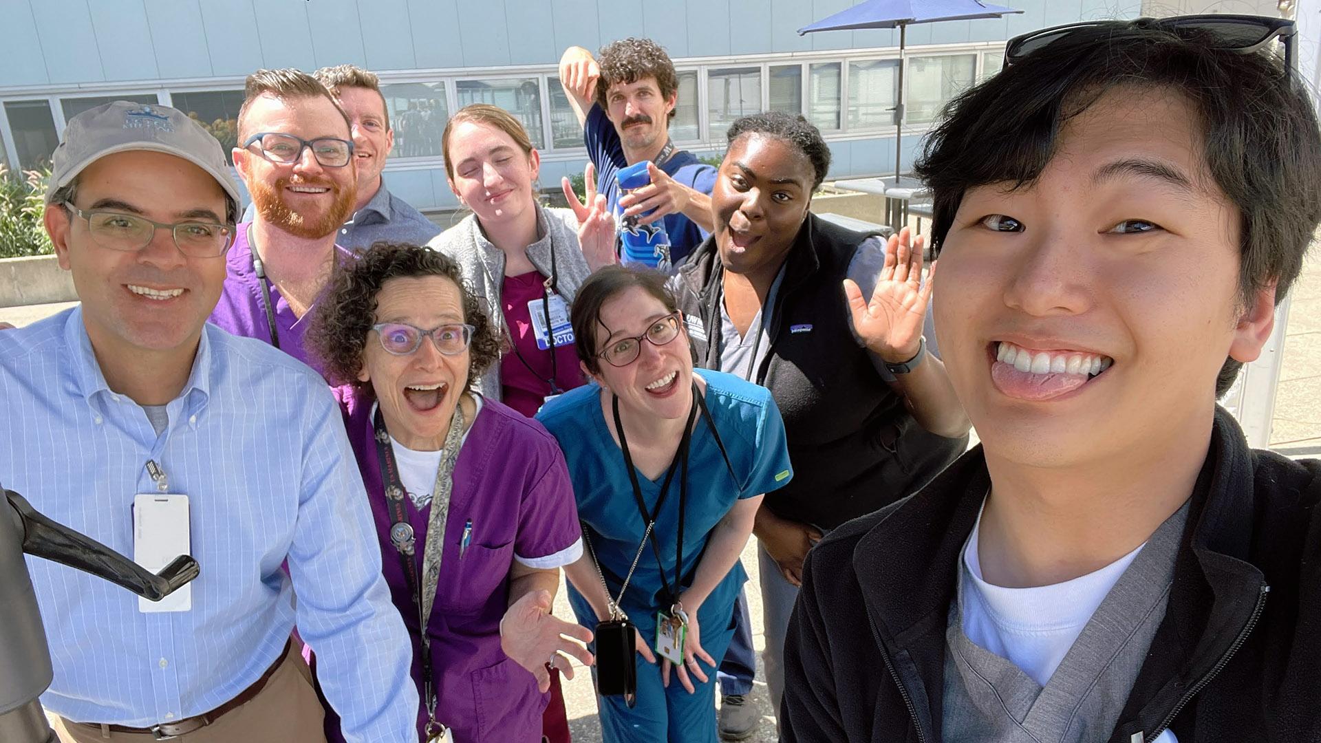 A group of residents in scrubs make silly faces outside the hospital. 