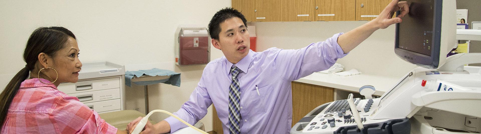 A doctor uses device on a patient's arm and points at a screen.