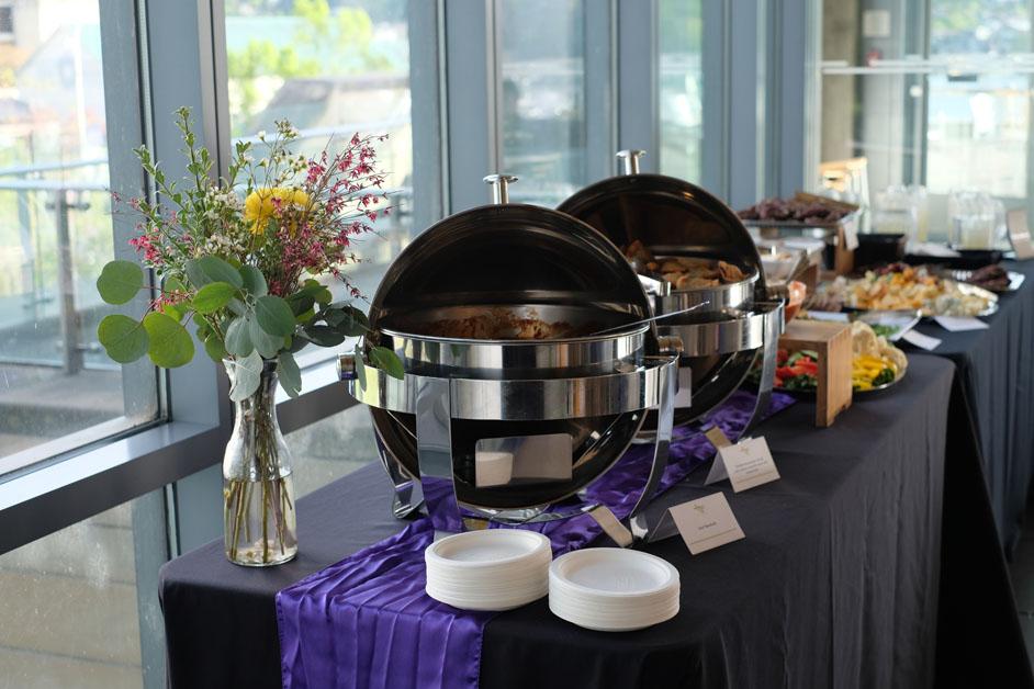 A buffet table, covered in a purple tablecloth. 