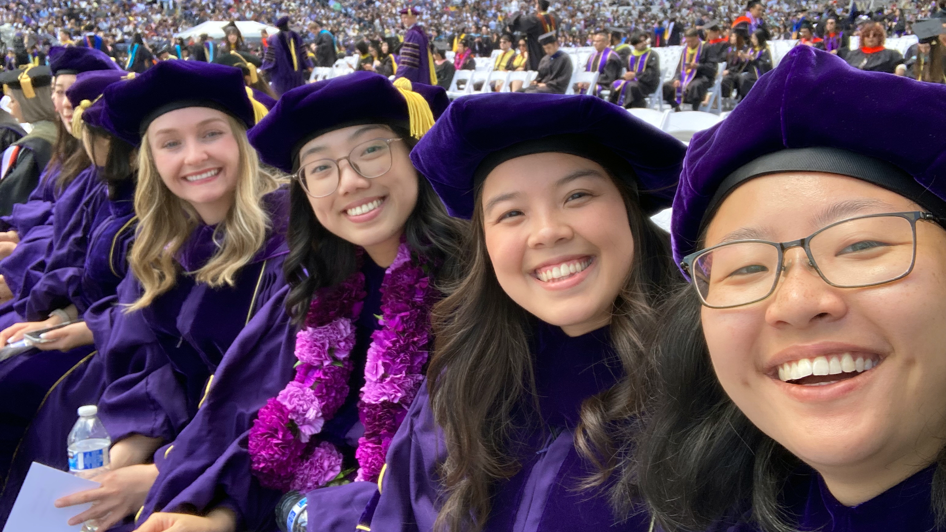 Graduates take a selfie in a crowded stadium.