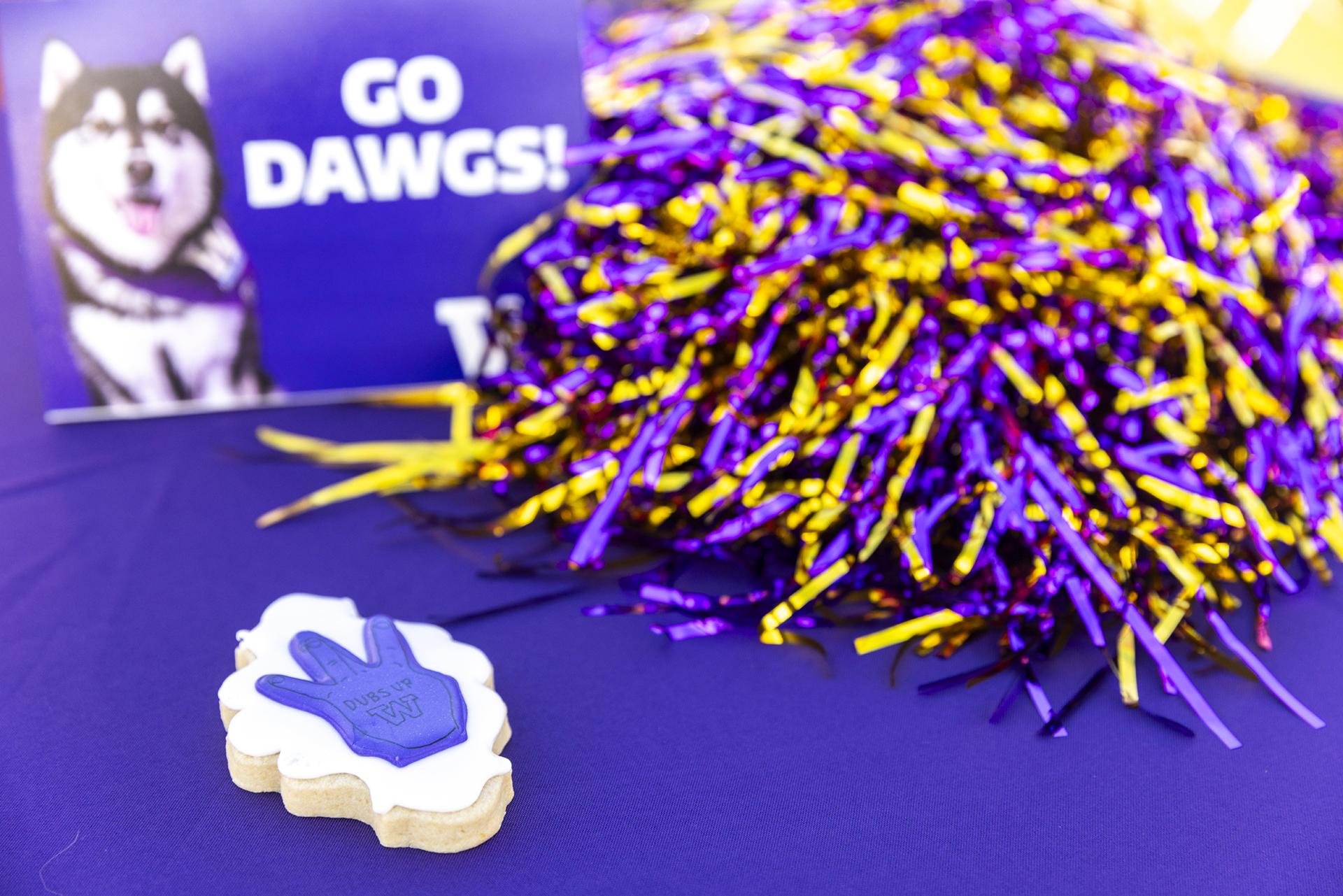 A pompom, a cookie, and picture of a fluffy husky with the caption "Go Dawgs" sit on purple tablecloth.