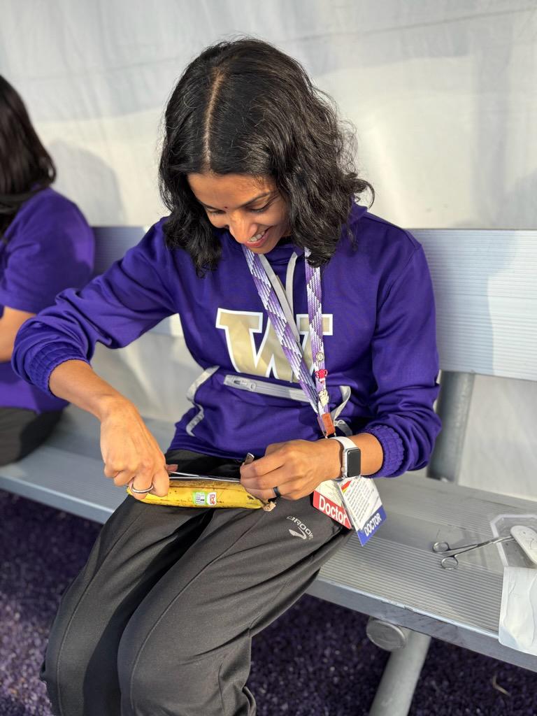 A woman in a purple sweatshirt practices sutures on a banana. 