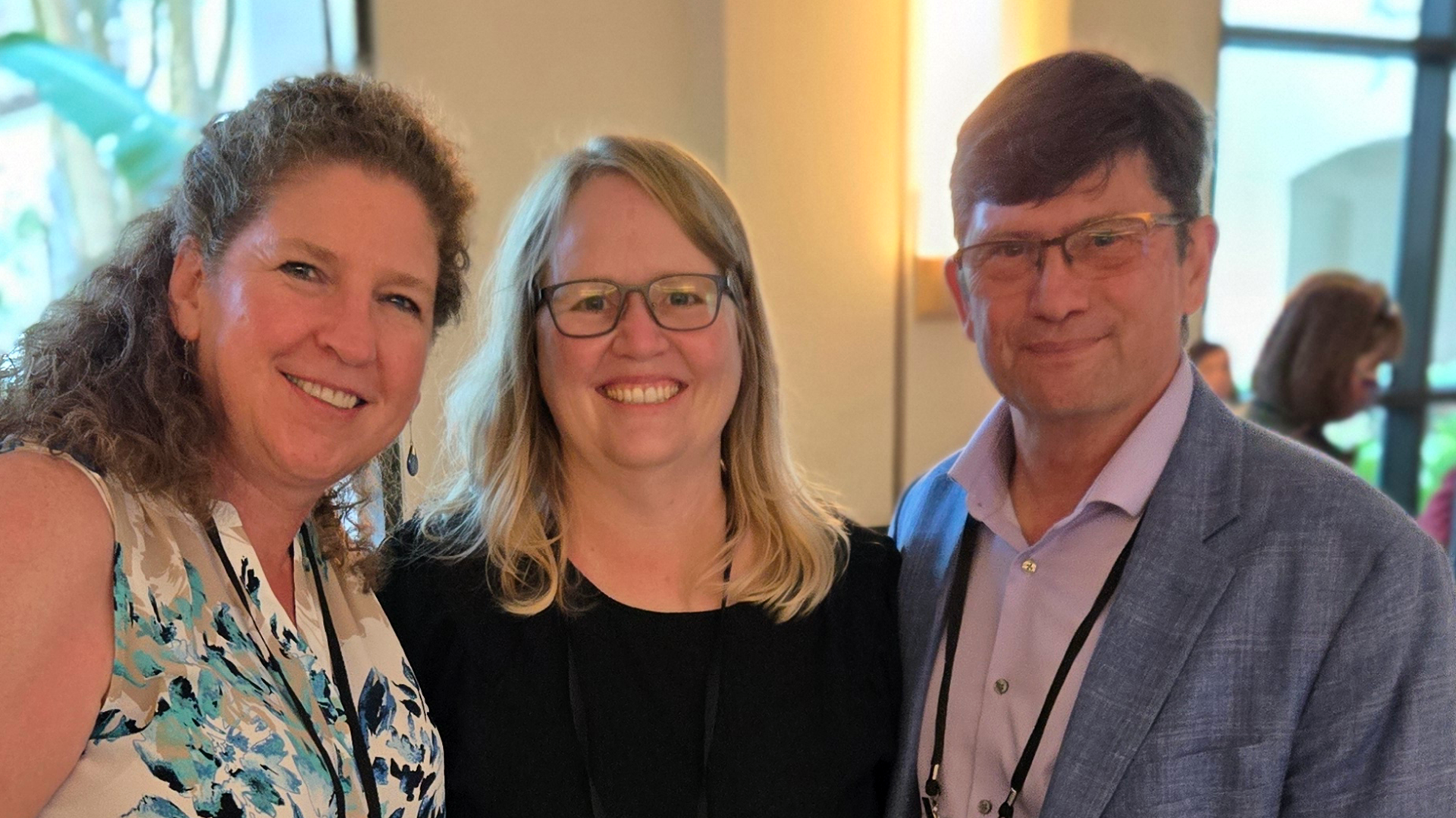 Three people smile at the camera in a conference room. 