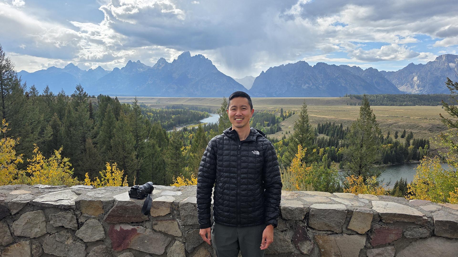 Dr. Matsuwaka in front of a vista of forest, fields, and mountains. 