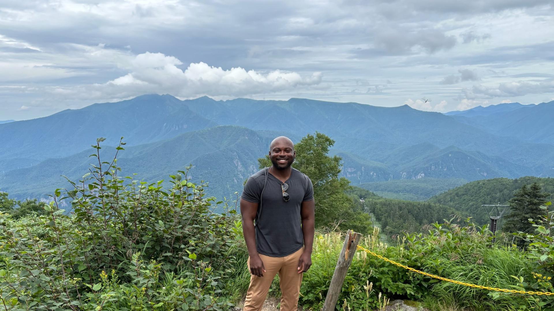 Dr. Sokunbi standing in front of a forested vista. 
