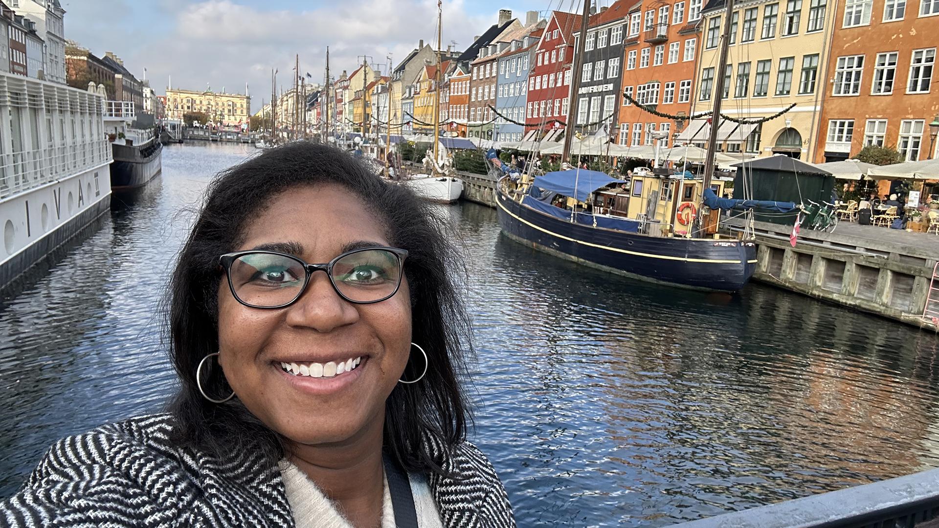 Dr. Booker smiles at the camera, in front of a waterway lined with colorful houses. 