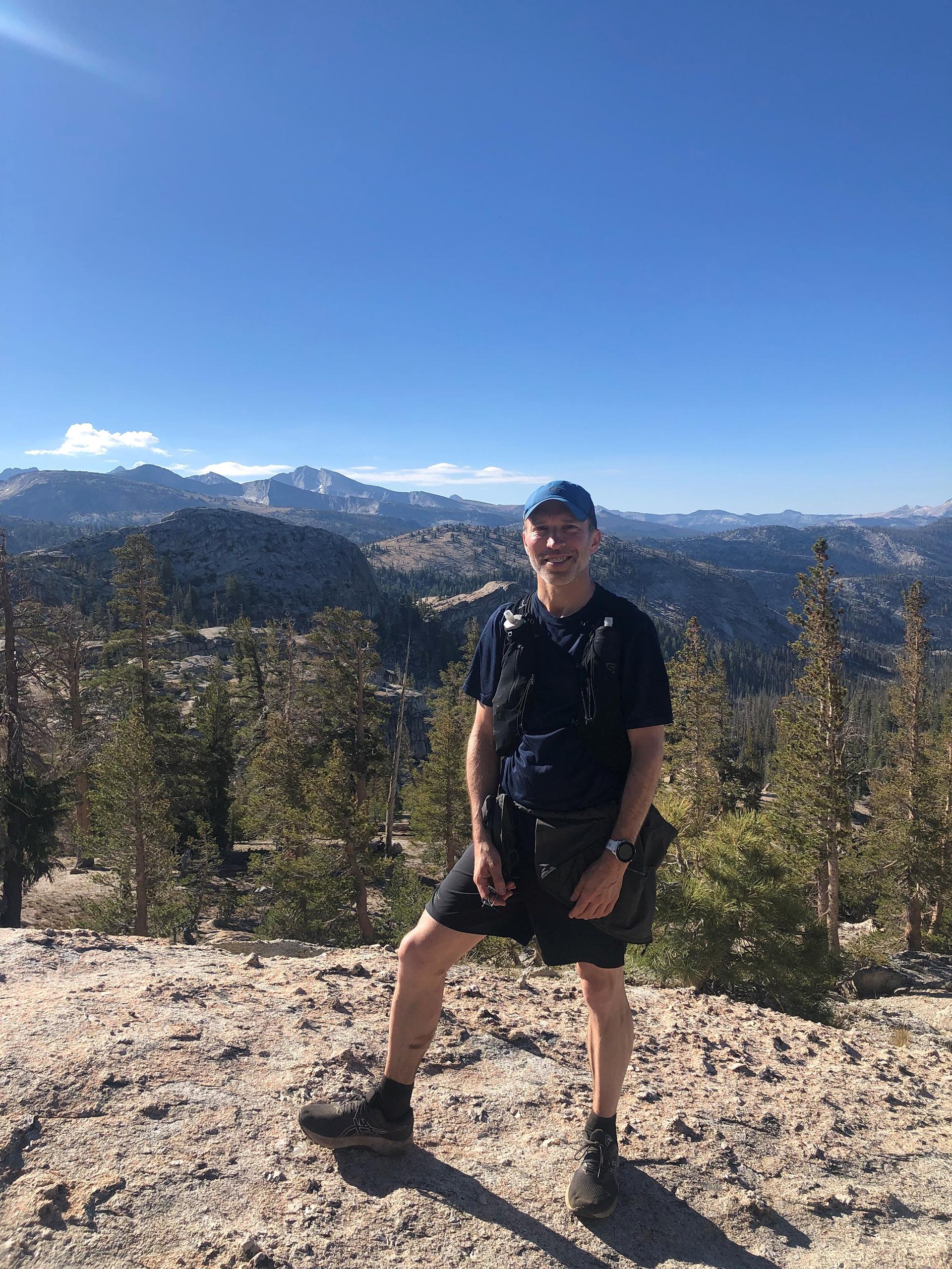 Dr. Harrast, in running gear, stands on a lookout point with forests and mountains stretching behind him. 