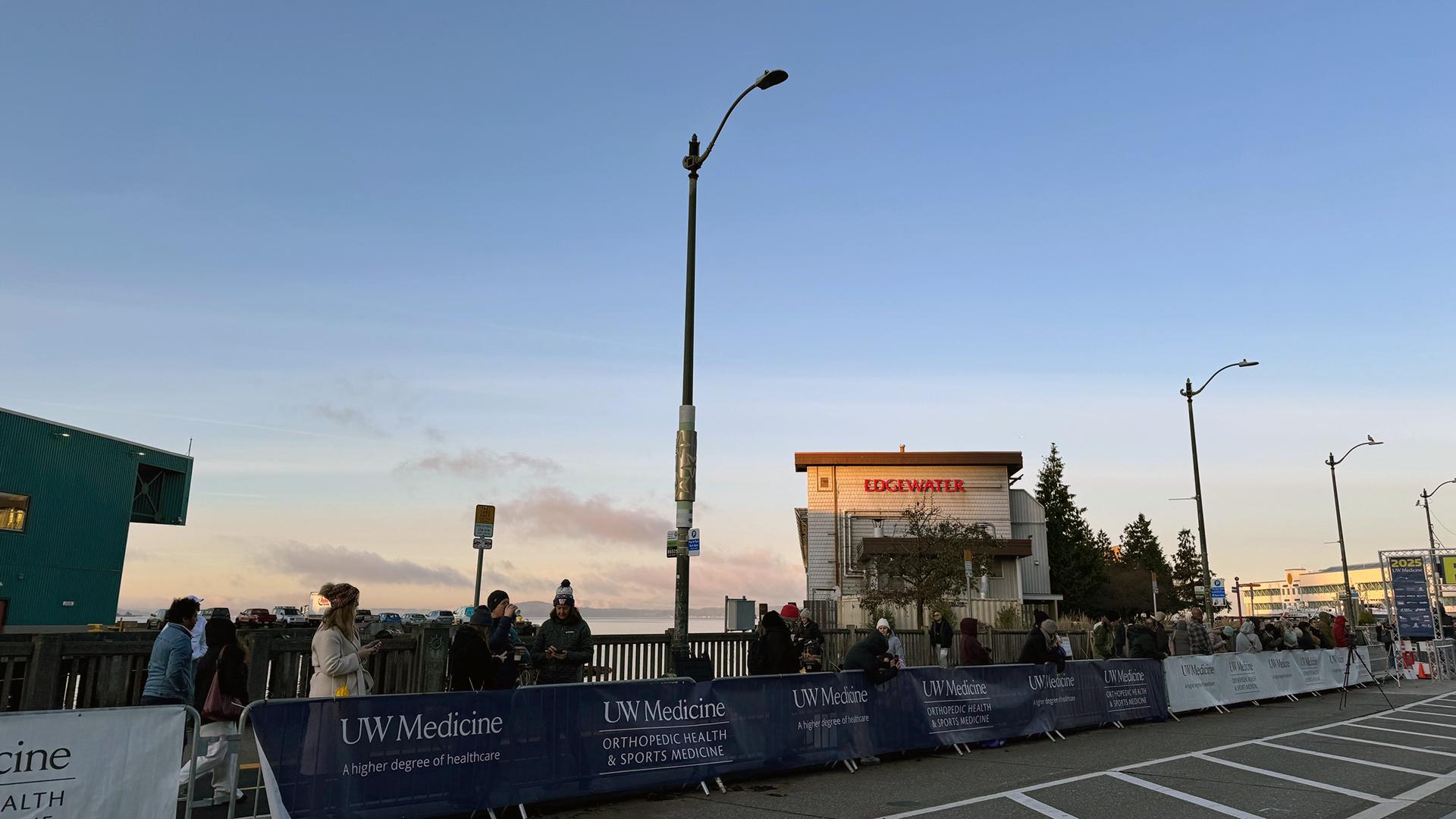 Spectators stand along a race route, with a deep blue sky behind them. 