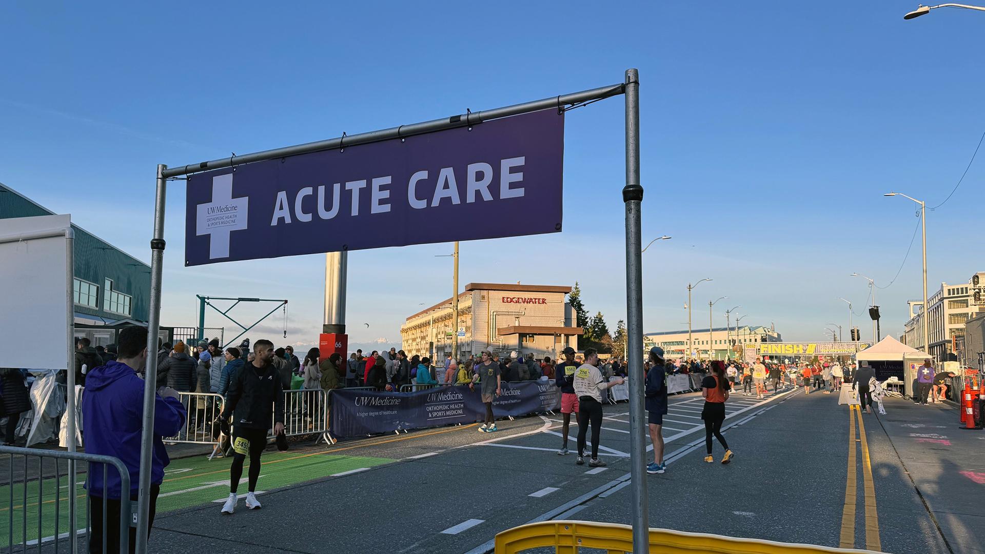 A purple banner saying "Accute Care" is in the forground, with the race finish line in the background. 