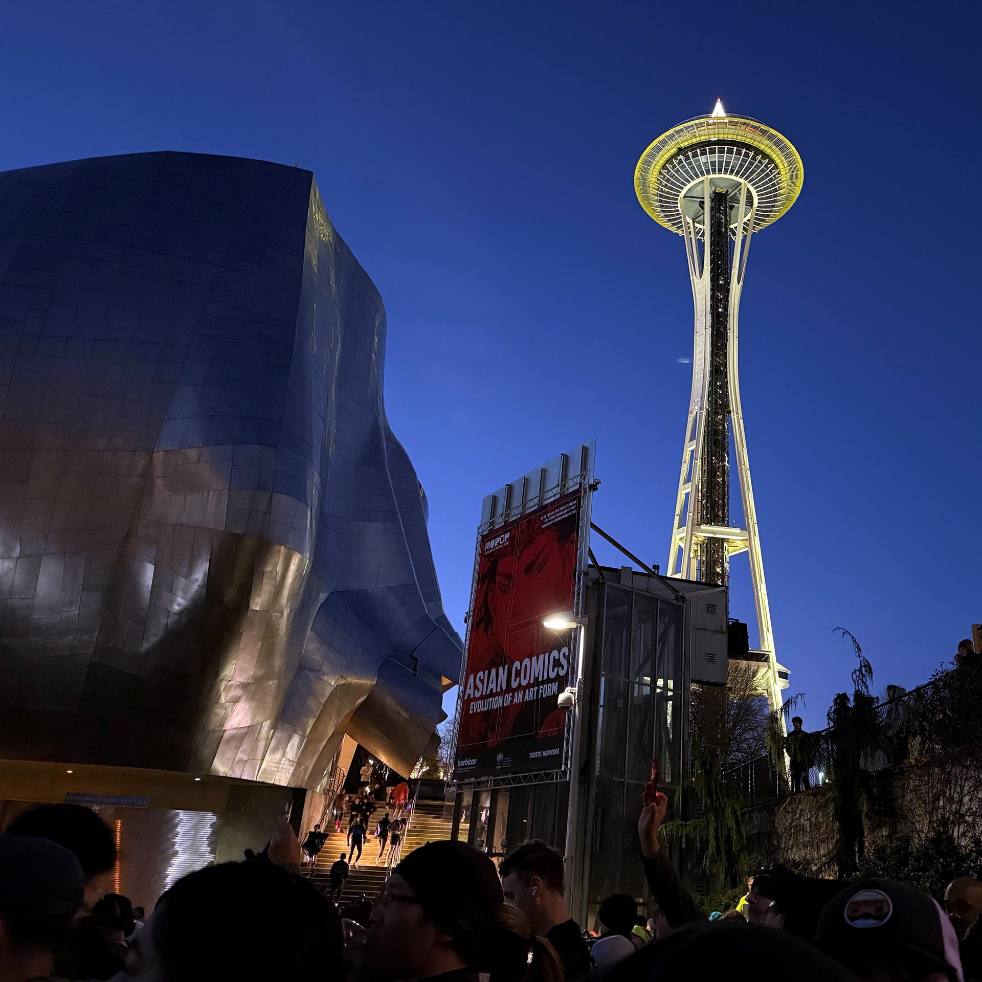 The Space Needle and MoPop shine against a dark sky, as runners wait to start running. 