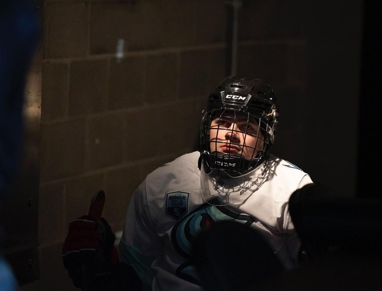 A boy wearing a hockey goalie mask and a Seattle Kraken jersey.