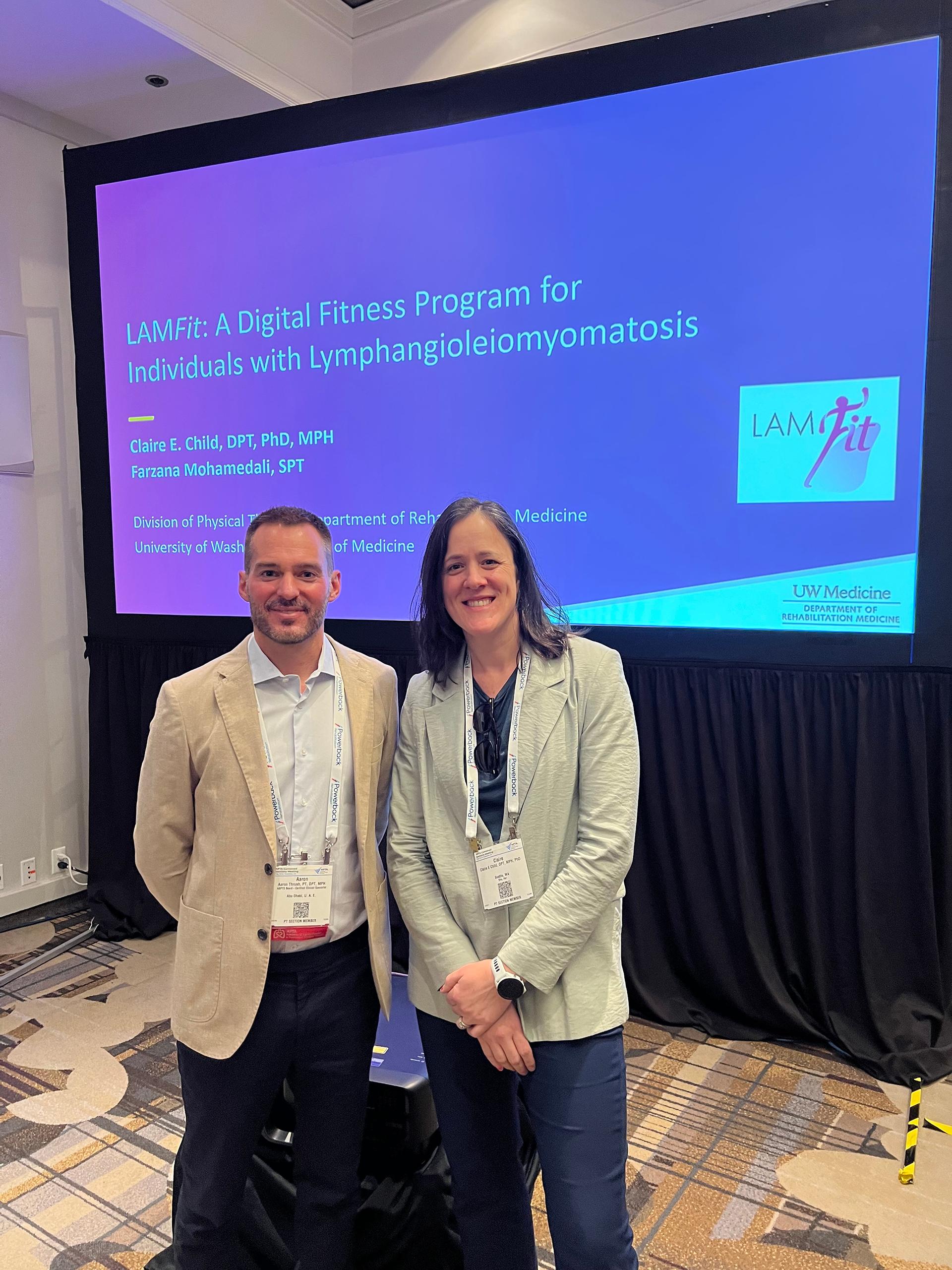 Two people stand together in front of a screen showing a presentation slide. 