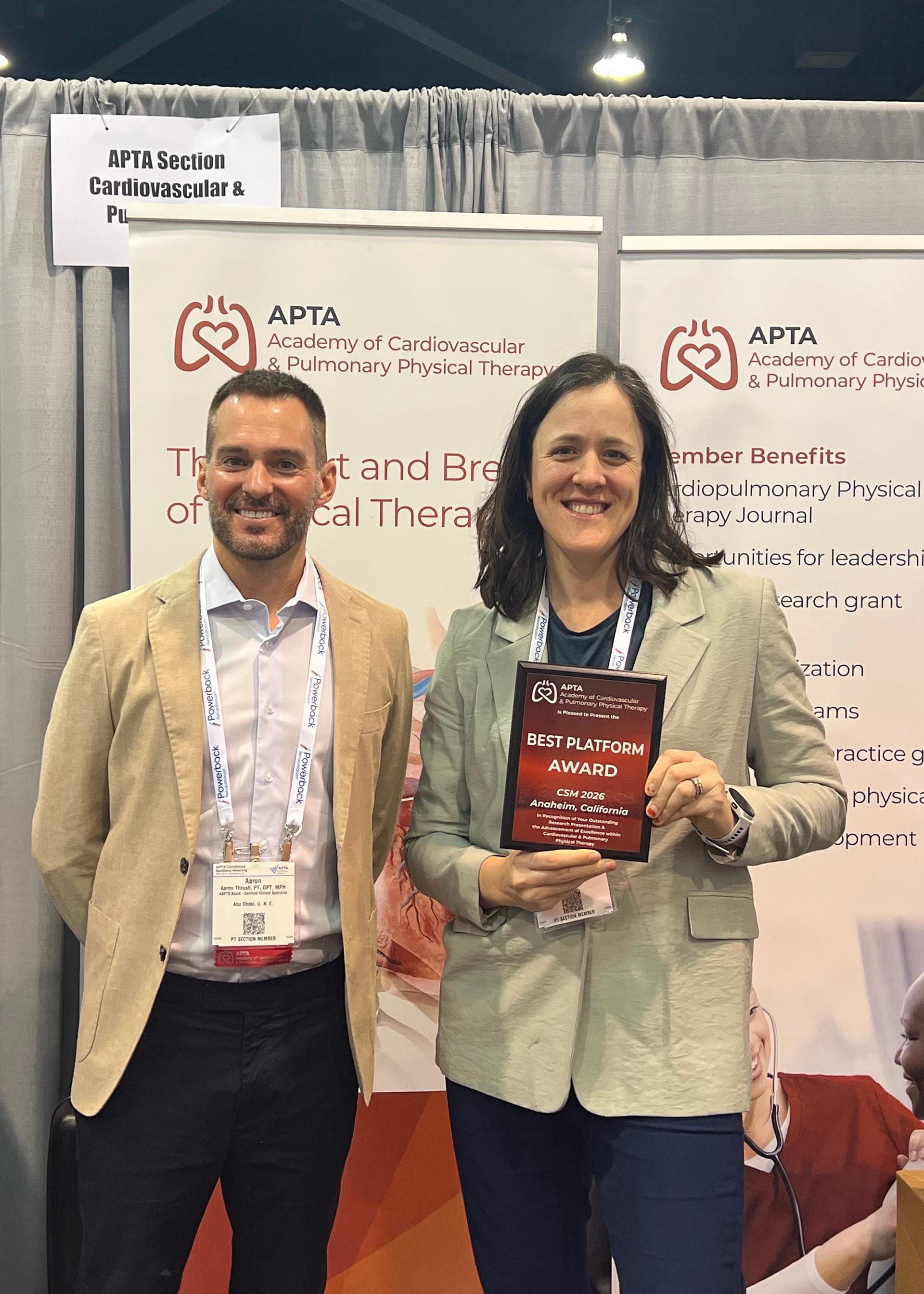 Two people stand together, one is holding an award. 