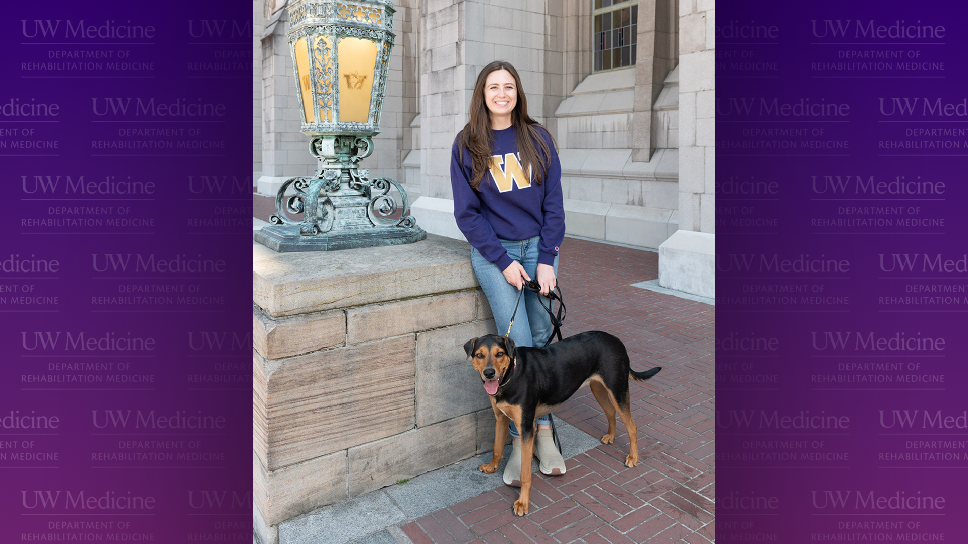 A woman in a purple shirt with a gold W holds the leach of a medium-size black and tan dog. 