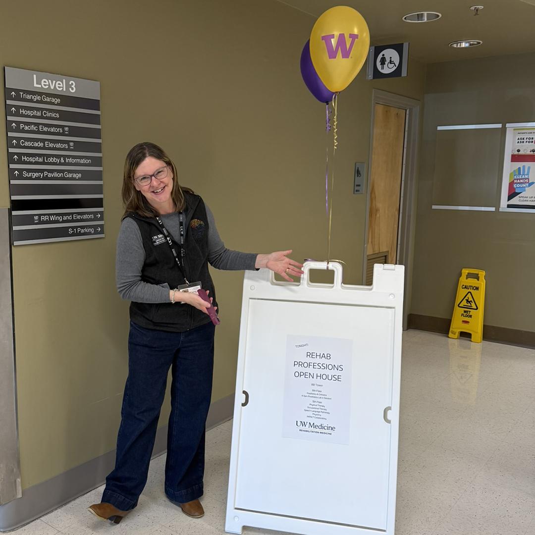 A woman stands next to a sandwich board with a sign promoting the rehabilitation medicine open house. 