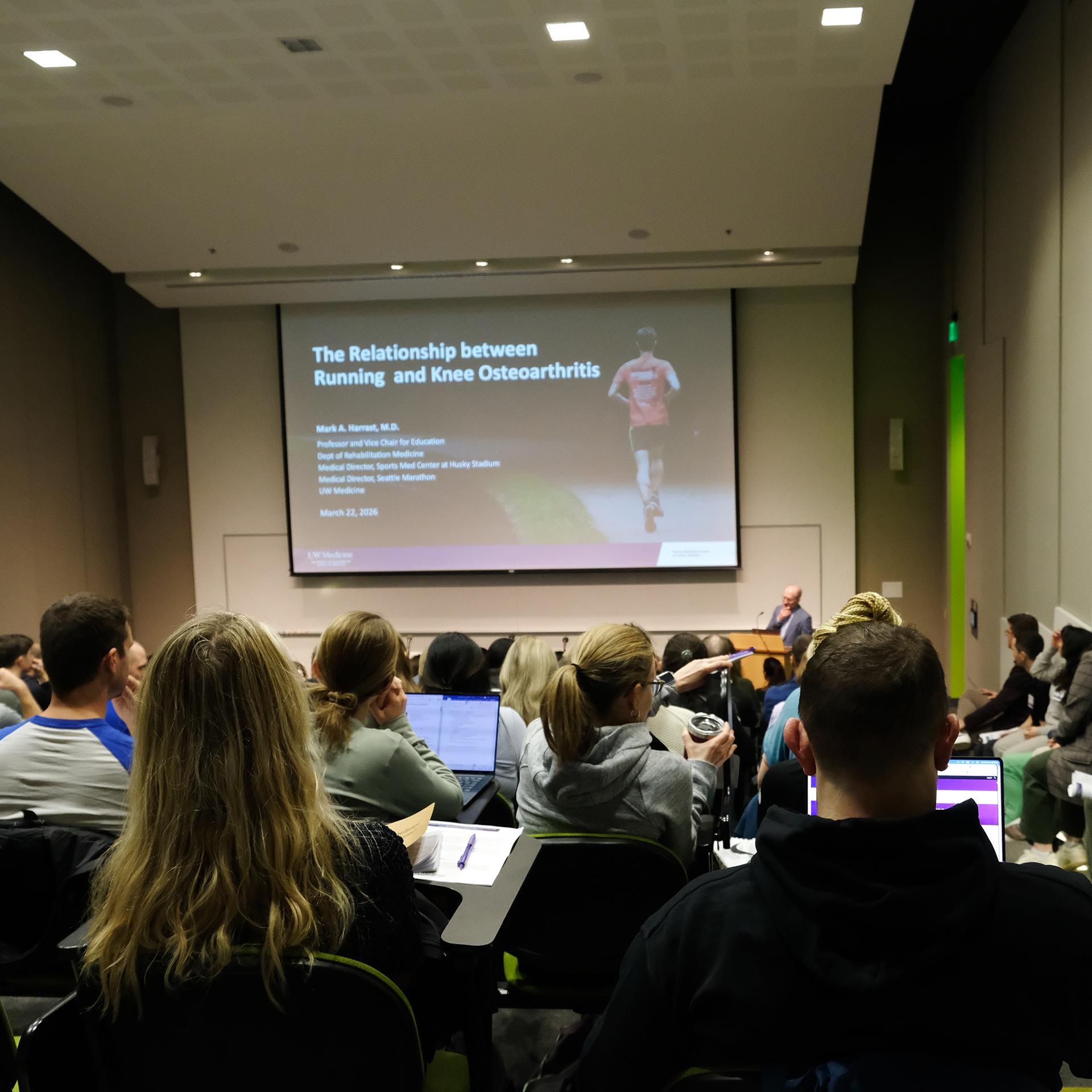 A crowd watches looks at a slide on the relationship between running and knee osteoarthritis. 