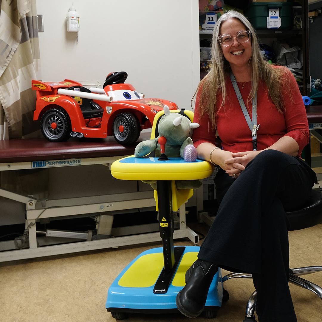 A woman sits next to colorful ride-on toys for children. 