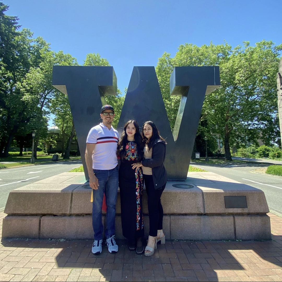 Three people stand in front of a W sculpture on a sunny day. 