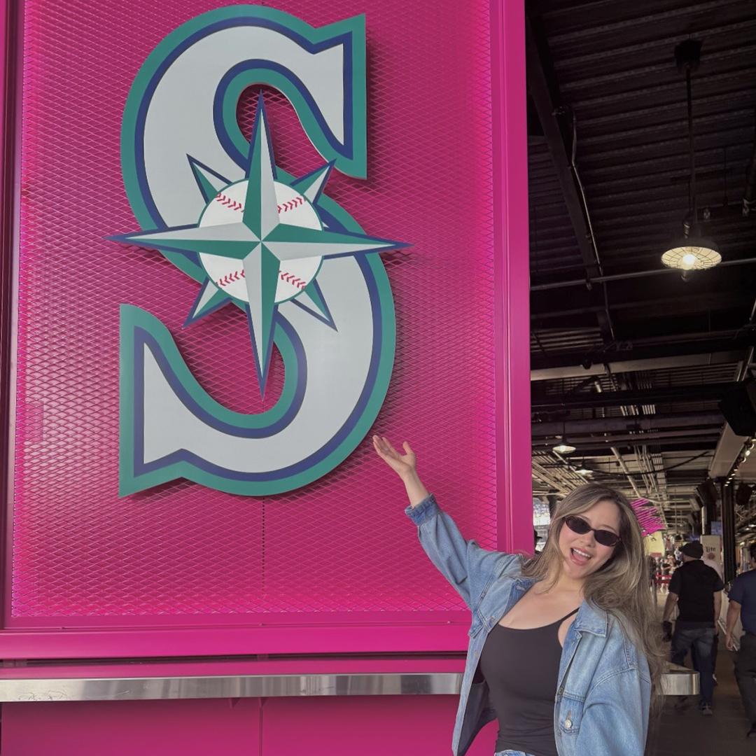 A woman stands under a pink sign with the Seattle Mariners logo. 