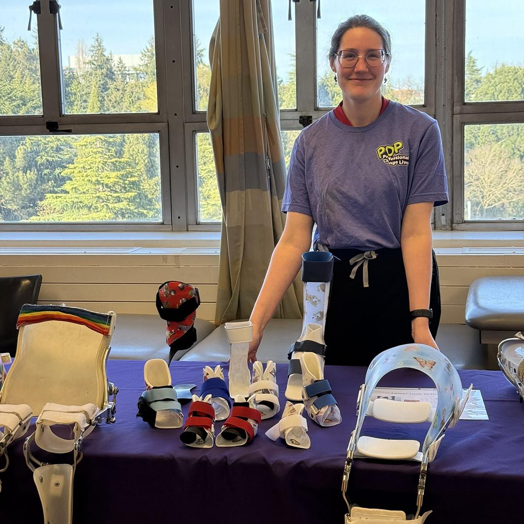 A woman stands at a table filled with various orthotic devices. 