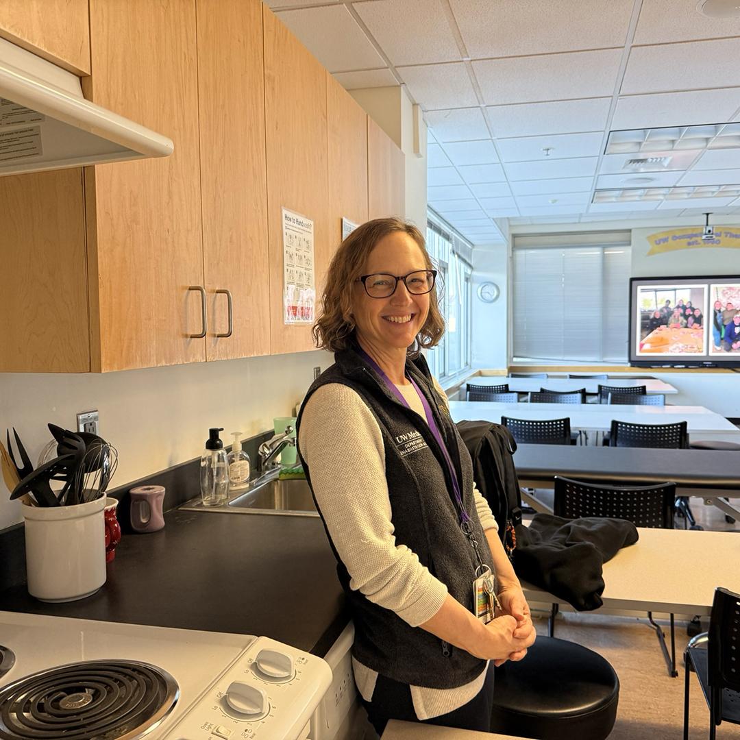 A woman smiles in a classroom that includes a demonstration kitchen. 