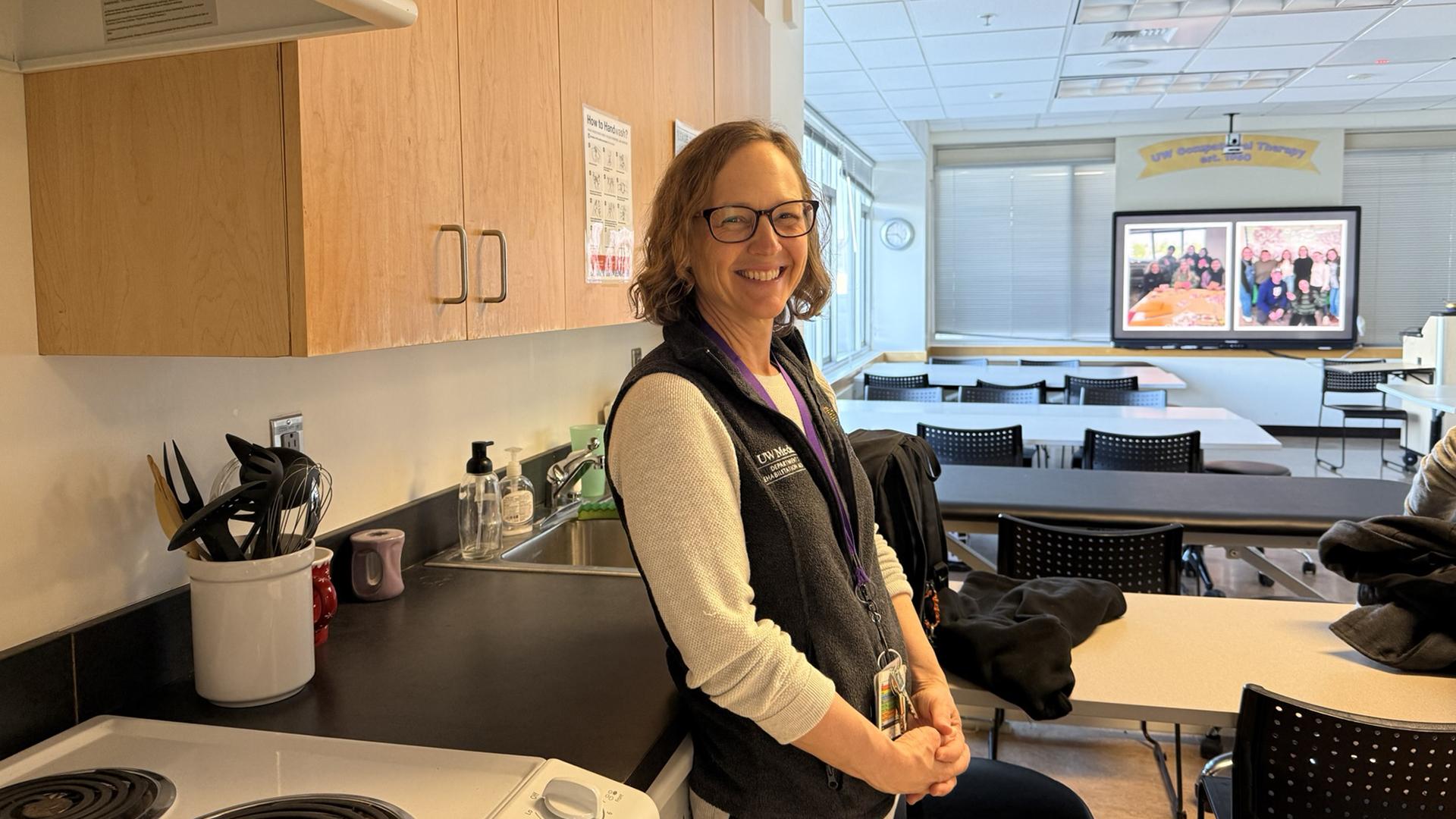 A woman stands smiling in a classroom fitted with a test kitchen. 