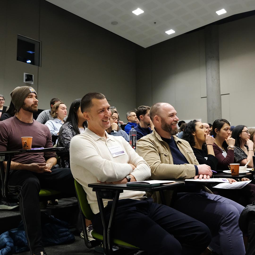 People in a full lecture hall smiling. 